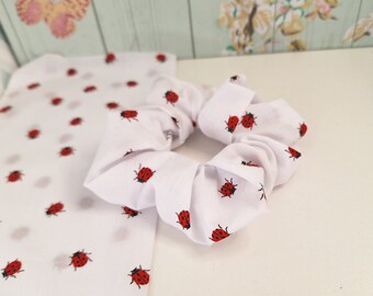May include: White scrunchie with a ladybug print. The scrunchie is made of fabric and has a gathered look.