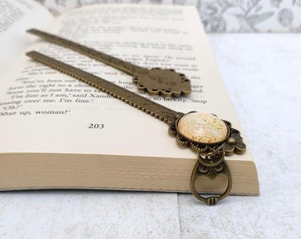 May include: A bronze bookmark with a ruler on one side and a decorative owl charm on the other. The owl charm has a white and gold patterned glass cabochon.