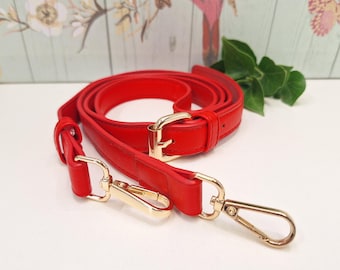 May include: A bright red adjustable bag strap featuring gold-toned metal hardware, including a rectangular buckle for length adjustment and two swivel lobster claw clasps at the ends for secure attachment to a handbag or accessory.