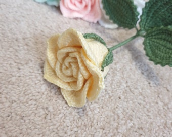 May include: Three crocheted roses in different colors: light green, pink, and yellow. The roses are arranged in a row on a beige surface.