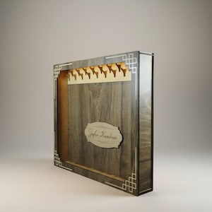 Könnte beinhalten: Holz-Ausstellungsbox mit dunkler Holzmaserung. Die Box hat ein dekoratives geometrisches Design an den Kanten und eine Reihe kleiner Haken im Inneren. Der Text "Jafar Kenbre" ist auf einer Holzplakette abgebildet.