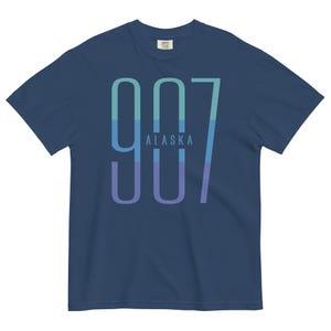 May include: A navy blue t-shirt featuring a graphic of the number 907 in a gradient of blue, green, and purple colours. The text "ALASKA" is printed in white below the number.