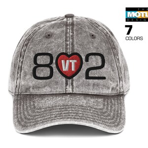May include: A gray baseball cap with the numbers "802" and a heart-shaped "VT" design. The cap has a distressed, vintage look. The text "7 COLORS" is visible on the right side of the cap.