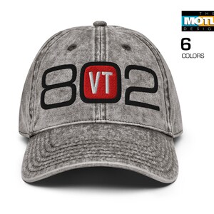 May include: A gray distressed baseball cap with black embroidered numbers "802" and a red embroidered square with the letters "VT" inside.