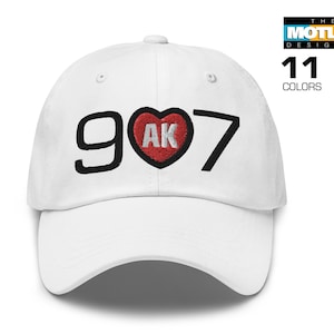 May include: White baseball cap with black embroidered text "907" and a red heart with white embroidered text "AK" in the centre.