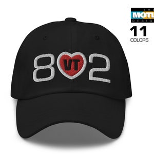 May include: Black baseball cap with white embroidered text "802" and a red heart with white "VT" inside. The Motley Designer.
