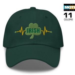 Pode incluir: Um boné de beisebol verde escuro com um trevo verde bordado e a palavra "IRISH" em amarelo. O trevo é cercado por um gráfico de batimento cardíaco amarelo.
