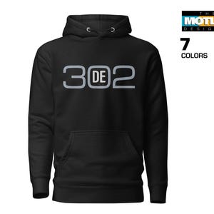 May include: Black hooded sweatshirt with a front pocket and drawstring hood. The sweatshirt features the text "3 DE 2" in a light gray font. The image also includes the text "7 COLORS" and the logo "THE MOTLEY DESIGNER".