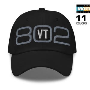 May include: Black baseball cap with embroidered "802 VT" in gray and white. The cap features a curved brim and a top button. The text "THE MOTLEY DESIGNER" and "11 COLORS" are also visible.