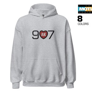 May include: A grey hooded sweatshirt with the text "907" in black with a red heart containing the letters "AK" in the centre.