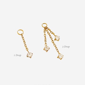 Peut inclure: Boucles d'oreilles dorées avec un design en chaîne. L'une a une seule goutte en forme de diamant, l'autre en a trois. Le texte "1 Drop" et "3 Drop" est visible sur l'image.
