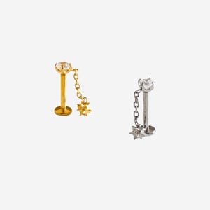 Può includere: Due piercing labret con base piatta. Uno è color oro con una gemma rotonda trasparente e un ciondolo a forma di stella appeso a una catenella. L'altro è color argento con una gemma rotonda trasparente e un ciondolo a stella abbinato.