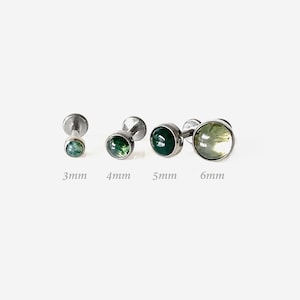 Può includere: Quattro borchie labret color argento con cabochon rotondi in agata muschiata verde. Le borchie sono disposte in fila, etichettate con le misure 3mm, 4mm, 5mm e 6mm, che indicano il diametro delle incastonature in pietra di ogni gioiello.