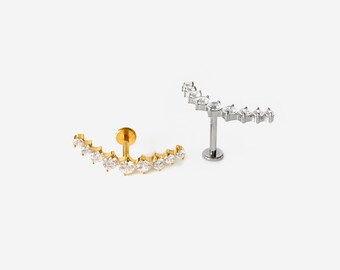 Può includere: Due piercing labret curvi con una fila di pietre trasparenti a taglio rotondo. Uno è color oro e l'altro color argento, entrambi con una base piatta. Il testo HYANGMI GU Jewelry è stampato nella parte inferiore dell'immagine.