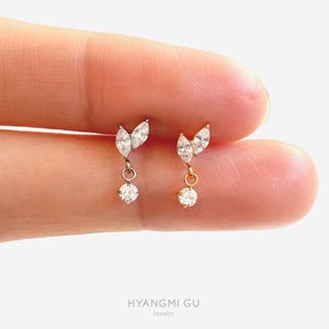 May include: Two delicate earrings featuring a marquise-cut crystal leaf design attached to a small circular crystal drop. One earring is set in silver-toned metal and the other in gold-toned metal. The text HYANGMI GU Jewelry is at the bottom.