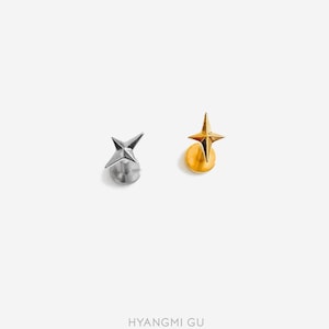 May include: Two flat-back stud earrings featuring a four-pointed star design. One earring is silver-toned metal, and the other is gold-toned metal. Each star has a faceted surface that comes to a sharp point, attached to a circular flat base.