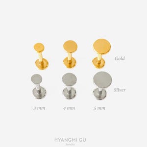 May include: A collection of six flat-back labret studs arranged in two rows. The top row features three gold-toned studs, and the bottom row features three silver-toned studs. Sizes are labelled as 3 mm, 4 mm, and 5 mm. Text reads Hyangmi Gu Jewelry.