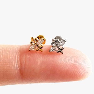 May include: Two stud earrings featuring a fleur-de-lis design, one in gold-tone metal and one in silver-tone metal. Each earring is accented with two marquise-cut clear stones arranged in a vertical pattern within the metal frame.