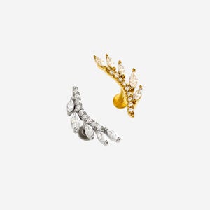 Könnte beinhalten: Zwei Ohrklemmen, eine goldfarbene und eine silberfarbene, jeweils mit marquiseförmigen Edelsteinen verziert. Die goldfarbene Manschette hat ein geschwungenes Design mit edelsteinen in einem blattartigen Muster angeordnet. Die silberfarbene Manschette spiegelt dieses Design wider.