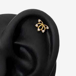 Könnte beinhalten: Ein goldfarbener Ohrstecker mit floralem Design. Der Stecker hat fünf klare, runde Edelsteine in einem filigranen, durchbrochenen Muster. Der Schmuck ist vor einem schwarzen Hintergrund platziert.