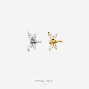 May include: Two dragonfly-shaped earrings, one silver and one gold, each featuring clear, marquise-cut gemstones. The earrings are set against a white backdrop. The brand name "HYANGMI GU Jewelry" is displayed at the bottom.