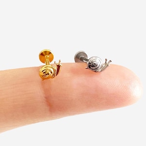 May include: Two small snail-shaped earrings. One is gold-coloured, and the other is silver-coloured. The earrings have a flat back and a post for piercing. The snail's body is detailed with a spiral shell and tiny antennae. These earrings are suitable for a variety of styles.