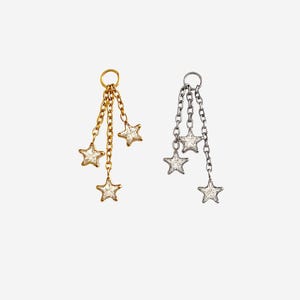 May include: Two dangling charms, one gold-toned and one silver-toned, each featuring three delicate chains of varying lengths. Each chain terminates in a small, five-pointed star encrusted with clear, sparkling stones attached to a circular jump ring.