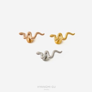 May include: Three snake-shaped stud earrings in rose gold, gold, and silver. The earrings are on a white background. The brand name "HYANGMI GU jewelry" is at the bottom.