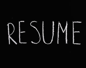 May include: The word "RESUME" written in white chalk on a black chalkboard.