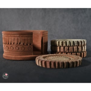 May include: Set of terracotta coasters with intricate designs. The coasters are stacked and feature a unique, decorative holder.