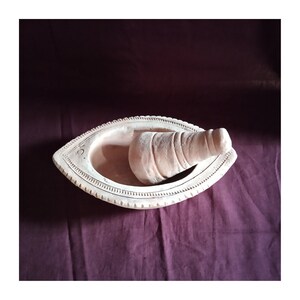 May include: A terracotta mortar and pestle set. The mortar is shaped like a boat and has a decorative design around the rim. The pestle is a cylindrical shape with a rounded end.