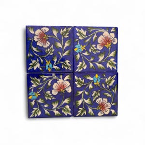 May include: Four square blue ceramic tiles with a floral design. Each tile features a repeating pattern of white and pink flowers, green leaves, and small yellow and blue accents. The tiles are arranged in a square formation.