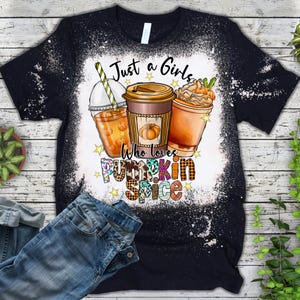 Może przedstawiać: Czarny T-shirt z wybielonym wzorem przedstawiającym trzy jesienne napoje i tekst "Just a Girls Who Loves Pumpkin Spice".
