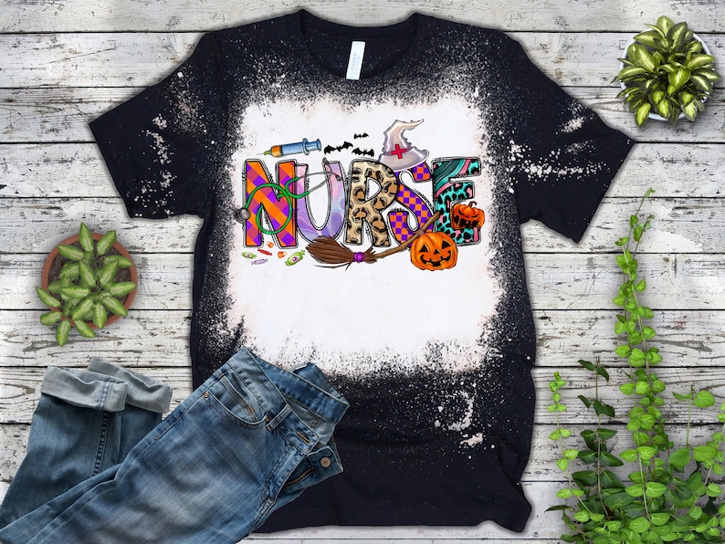 Pu&ograve; includere: Una maglietta nera con un design spruzzato di candeggina che presenta la parola "NURSE" in lettere colorate con accenti a tema Halloween, tra cui un cappello da strega, una scopa e zucche.