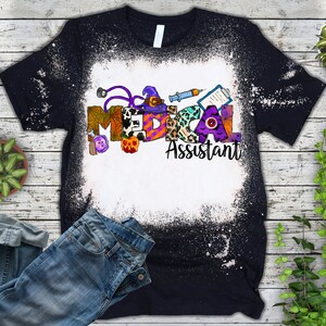 May include: A black t-shirt with a white bleach design featuring the words "Medical Assistant" with Halloween-themed letters and icons.