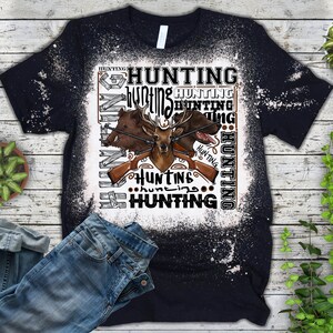 May include: A black t-shirt with a white bleach design featuring a deer, two boar, and rifles. The design includes the word "hunting" repeated multiple times.