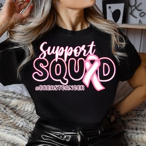 Peut inclure: T-shirt noir avec l'inscription "Support Squad" en rose et blanc, orné d'un ruban rose et du hashtag #BREASTCANCER. Le t-shirt est de style col rond.