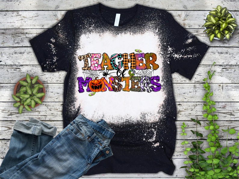 May include: Black t-shirt with a bleach-splattered design. The shirt features a colorful graphic that says "Teacher of Monsters" with a spider and a pumpkin.