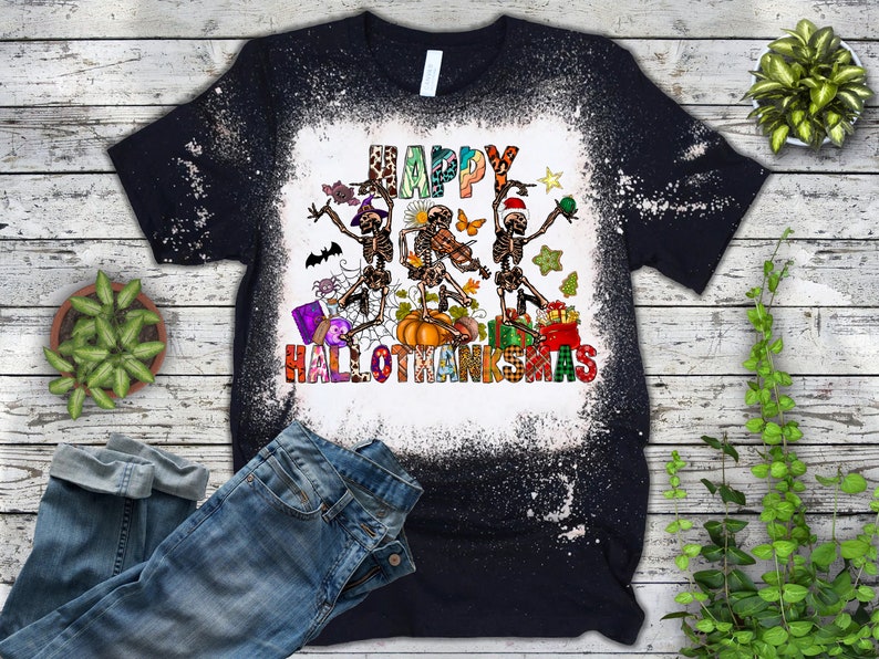 May include: A black t-shirt with a bleach-splattered design featuring three skeletons dancing with the text "Happy Hallothanksmas".