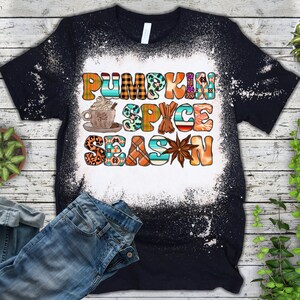 May include: Black t-shirt with a white bleach design that says "Pumpkin Spice Season" in colourful letters. The design includes a cup of coffee, cinnamon sticks, and a star anise.