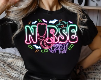 Puede incluir: Camiseta negra con un gráfico de neón rosa, verde y azul de un estetoscopio y la palabra "NURSE" con murciélagos y píldoras alrededor.