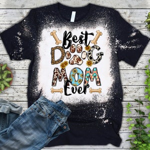 以下が含まれることがあります： 「Best Dog Mom Ever」と書いてある、漂白されたデザインの黒いTシャツ。デザインには、ヒョウ柄、牛柄、ひまわりなど、さまざまなパターンが施された肉球のプリントが施されています。