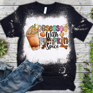 May include: A black t-shirt with a white bleach design. The design features a cup of pumpkin spice latte, pumpkins, and the text "Obsessed with Pumpkin Spice".
