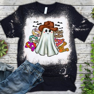 Puede incluir: Una camiseta negra con un dise&ntilde;o salpicado de lej&iacute;a que presenta un fantasma con un sombrero de vaquero y la palabra "Boo-Haw" en letras de colores.