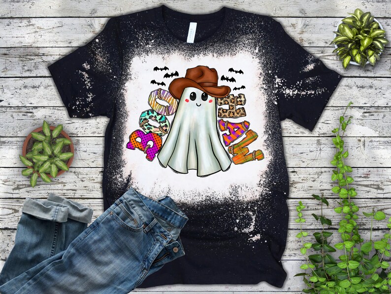 Puede incluir: Una camiseta negra con un dise&ntilde;o salpicado de lej&iacute;a que presenta un fantasma con un sombrero de vaquero y la palabra "Boo-Haw" en letras de colores.