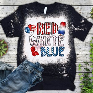 Puede incluir: Una camiseta negra con un dise&ntilde;o de blanqueador blanco que dice "Red White & Blue" con estrellas y rayas rojas, blancas y azules. Tambi&eacute;n hay globos rojos, blancos y azules y una paleta de hielo en el dise&ntilde;o.