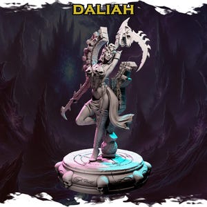 Op de afbeelding: Een wit geverfd miniatuurbeeldje van een vrouwelijke figuur met een schedelvormige hoofdtooi en een grote zeis. De figuur staat op een ronde basis met schedels rond de rand. De basis is geschilderd in tinten grijs en blauw.