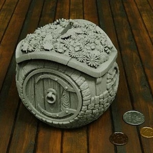 Könnte beinhalten: Ein rundes, graues Dekorationshaus mit einer Tür und einem Dach, das mit Blumen bedeckt ist. Das Haus ist aus einem strukturierten Material gefertigt und hat einen rustikalen Look.