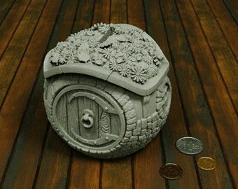 May include: A gray, round, decorative house with a door and a roof covered in flowers. The house is made of a textured material and has a rustic look.