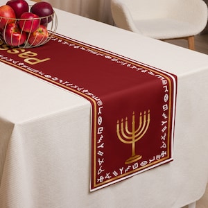 May include: A red table runner with a gold menorah design and Hebrew text. The runner has a white border with gold trim. The text on the runner reads "Passover".